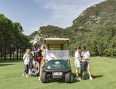eine Gruppe von Personen, die auf einem Golfplatz um einen Golfwagen herumsteht